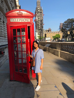 A picture of Alejandra standing in the sunshine beside one of London's famous red telephone boxes.